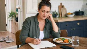 An adult reviewing a wellness journal and balanced meal while considering why weight loss can be difficult