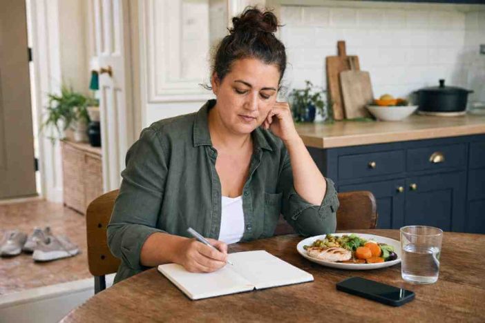 An adult reviewing a wellness journal and balanced meal while considering why weight loss can be difficult